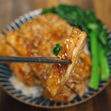 Chopsticks holding a piece of honey garlic chicken with sesame seeds and bok choy