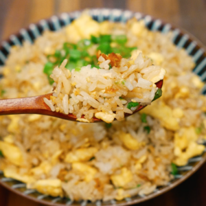 Close-up of egg fried rice on a wooden spoon with fluffy scrambled eggs and scallions