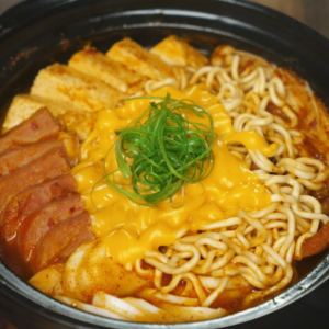 Korean army stew (budae jjigae) with ramen noodles, spam, tofu, cheese, and scallions in a hot pot