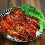 A full view of a BBQ gochujang chicken rice bowl featuring thick slices of caramelized chicken glazed in a spicy, sweet, and smoky Korean-style sauce. Nestled over fluffy white rice and accompanied by blanched bok choy, this dish balances heat and freshness in a visually vibrant and satisfying dinner perfect for Asian recipe lovers.