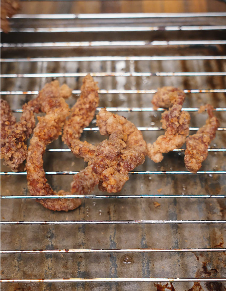 Freshly fried strips of crispy beef resting on a wire rack to drain excess oil, showcasing a golden, crunchy texture perfect for tossing in sauce.