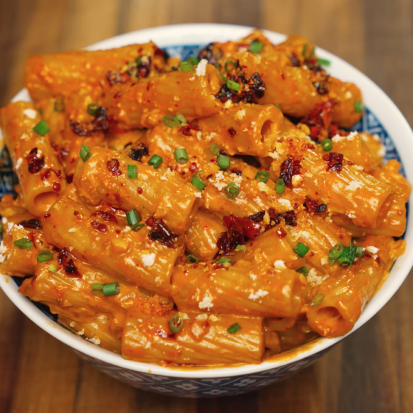 Full bowl of rigatoni coated in creamy chili oil vodka sauce, topped with chili crisp, parmesan, and fresh chives — rich and spicy pasta dish.
