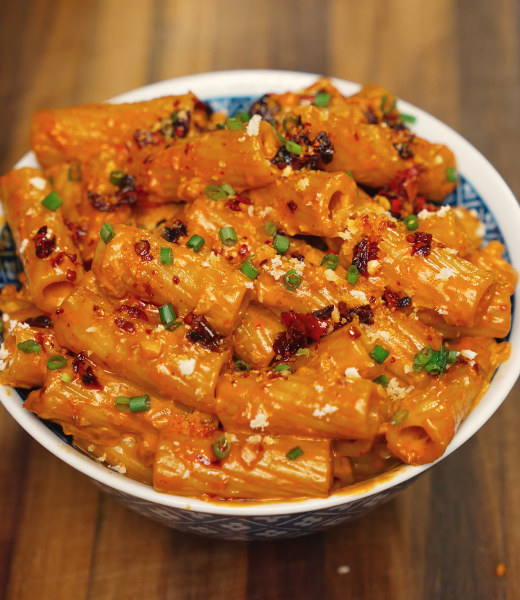 Full bowl of rigatoni coated in creamy chili oil vodka sauce, topped with chili crisp, parmesan, and fresh chives — rich and spicy pasta dish.