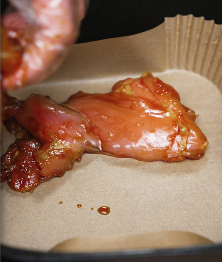 Marinated chicken thigh placed in an air fryer with parchment — perfect for air fryer chicken bulgogi recipes.