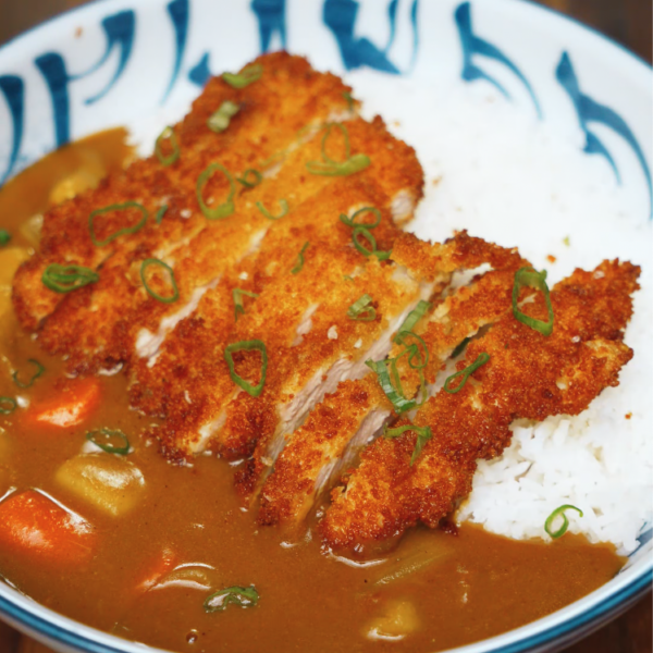 Sliced chicken katsu served over fluffy white rice and topped with Japanese curry sauce – classic chicken katsu curry bowl garnished with scallions.