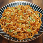 Bowl of chili garlic butter noodles garnished with sesame seeds, red pepper flakes, and sliced scallions — quick and easy spicy noodle recipe.