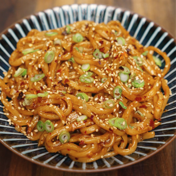 Bowl of chili garlic butter noodles garnished with sesame seeds, red pepper flakes, and sliced scallions — quick and easy spicy noodle recipe.