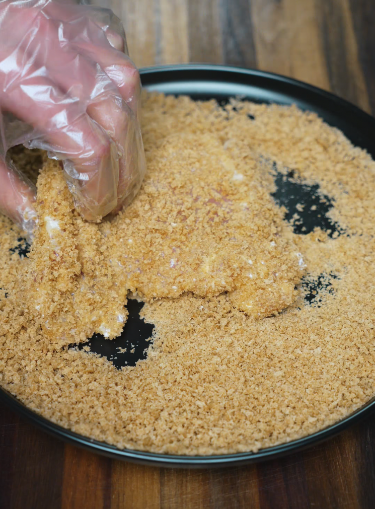 Boneless chicken thigh being coated in golden panko breadcrumbs for crispy chicken katsu – essential step for homemade chicken katsu curry.
