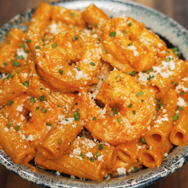 A bowl of rigatoni tossed in a spicy, creamy sauce with perfectly cooked shrimp, finished with parmesan and chives. The vibrant orange color and creamy texture make this a bold, comforting pasta dish.
