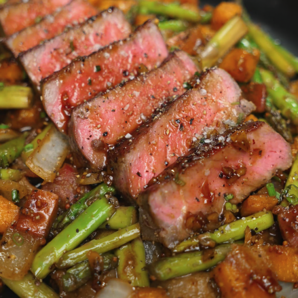 A close-up of a fork holding a perfectly cooked slice of steak above a bed of glazed vegetables. The steak’s interior is tender and rosy while the outer layer is seared for maximum flavor.