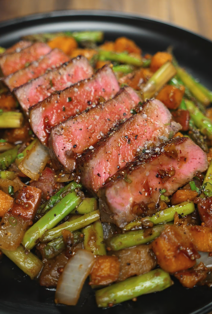 A close-up of a fork holding a perfectly cooked slice of steak above a bed of glazed vegetables. The steak’s interior is tender and rosy while the outer layer is seared for maximum flavor.