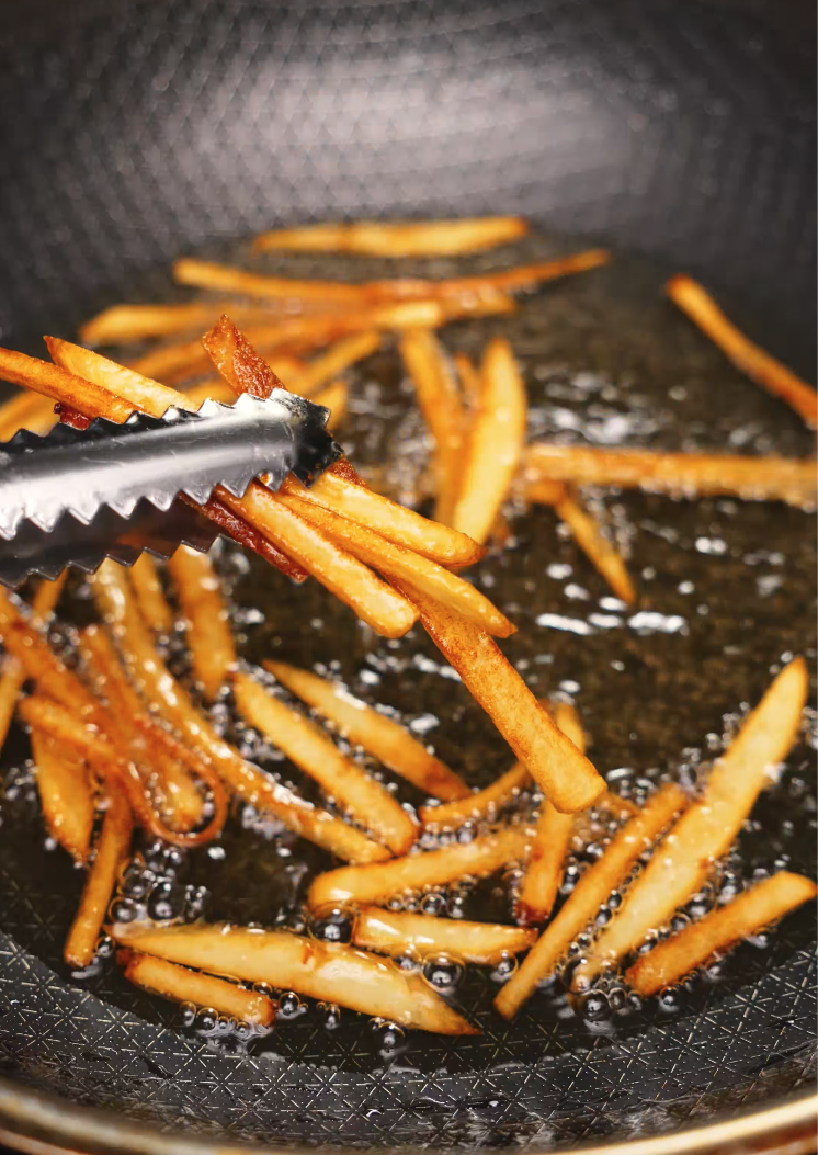 Golden five-spice French fries being lifted out of bubbling oil with metal tongs.