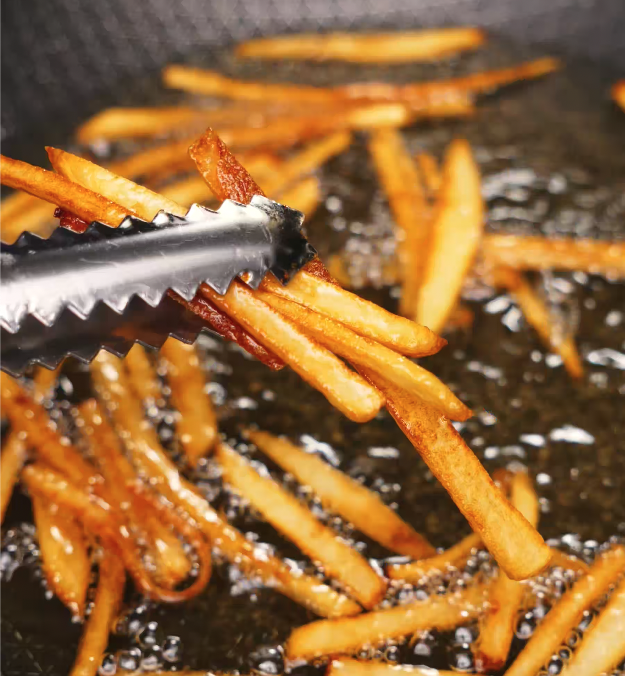 Golden five-spice French fries being lifted out of bubbling oil with metal tongs.