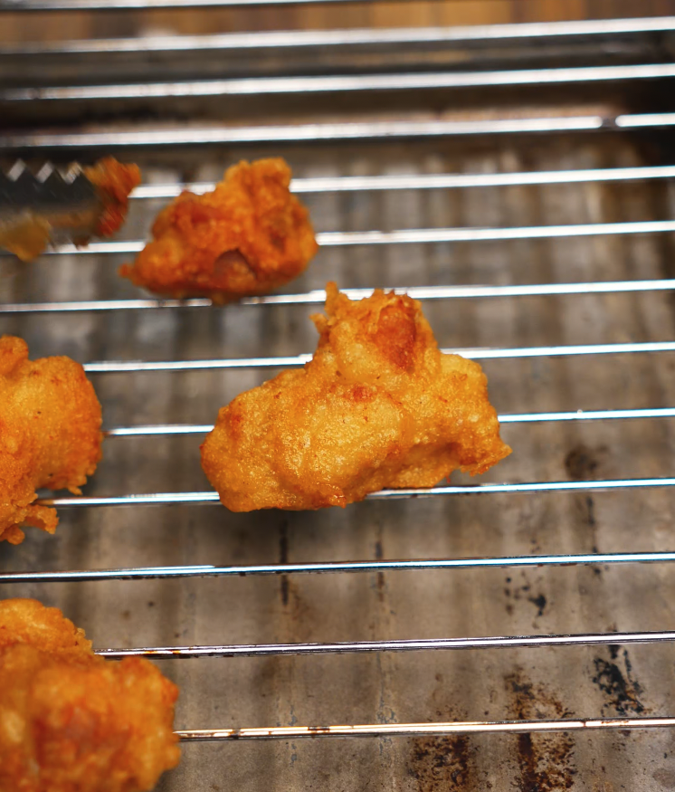 Golden brown pieces of fried chicken resting on a wire rack to maintain their crispy texture, fresh out of the fryer and ready to be coated in sauce.