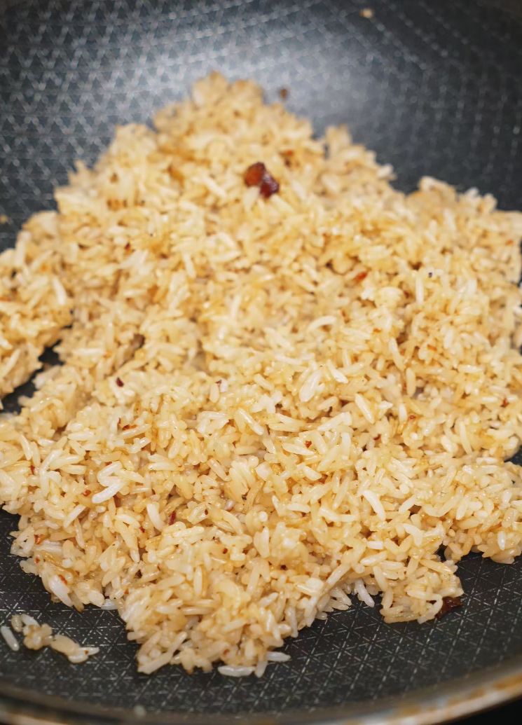 A pan filled with golden brown garlic butter fried rice, evenly stir-fried and infused with aromatic garlic butter and seasonings. The individual grains are separated and glistening with oil, indicating perfect texture and moisture. Ideal for those looking for a quick, easy Asian dinner made with leftover rice, this dish offers intense umami flavor with minimal ingredients.