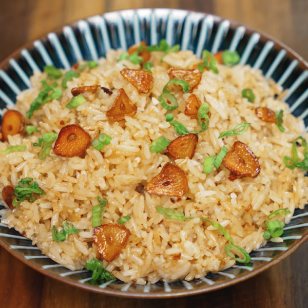 A finished bowl of garlic butter fried rice garnished with crispy golden garlic chips and chopped green onions. The fluffy, flavorful rice is glistening with garlic butter, delivering a savory and comforting dish ideal for meal prep or a quick weeknight dinner. This visually appealing bowl highlights the simplicity and bold flavors of a popular Asian comfort food.