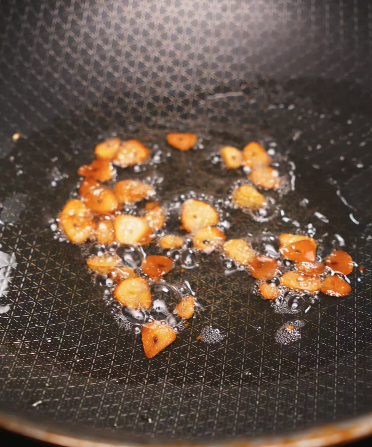 Thinly sliced garlic pieces frying in hot oil in a non-stick skillet, turning golden brown and crispy. These garlic chips add crunch and intense flavor to garlic butter fried rice and are a key component in authentic Asian-inspired rice dishes. This step enhances the aroma and depth of flavor, making the dish irresistible.