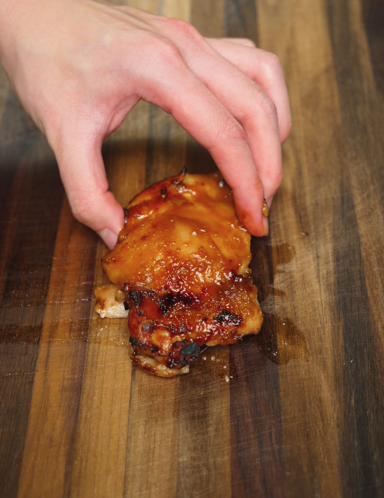 A freshly grilled miso-glazed chicken thigh rests on a wooden cutting board, showcasing caramelized edges and glistening glaze from the broiler or air fryer.