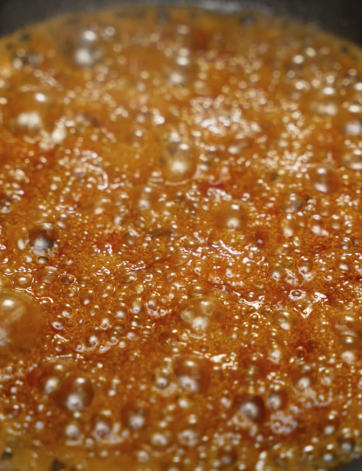 Thick honey butter sauce simmering and bubbling in a pan, highlighting the rich, glossy texture of the sweet-savory glaze. This sauce is made from butter, honey, and a hint of spice, perfect for coating crispy chicken tenders or other Southern-inspired dishes.