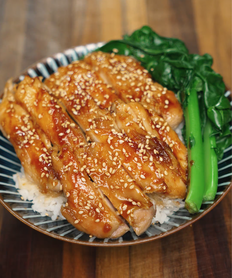 A bowl of sliced honey garlic chicken served over steamed jasmine rice with sautéed Chinese broccoli (gai lan). The chicken is coated in a glossy honey garlic glaze and topped with sesame seeds for texture and added flavor. This protein-packed Asian rice bowl is perfect for lunch, dinner, or quick meal prep recipes.
