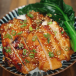 A finished miso glazed chicken bowl with sliced chicken over steamed rice, garnished with sesame seeds, scallions, and a side of vibrant green bok choy.