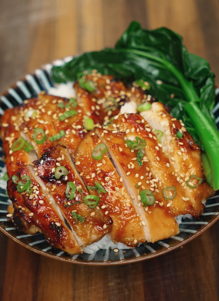 A finished miso glazed chicken bowl with sliced chicken over steamed rice, garnished with sesame seeds, scallions, and a side of vibrant green bok choy.