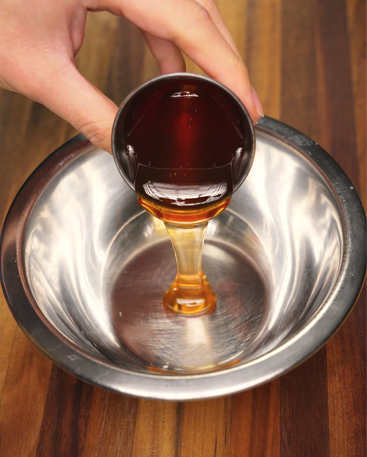 A stream of golden honey being poured into a stainless steel mixing bowl, one of the essential ingredients for making homemade honey garlic chicken glaze. The rich amber color and syrupy consistency hint at the sweetness that balances the savory garlic soy flavors in this quick and easy Asian chicken marinade.