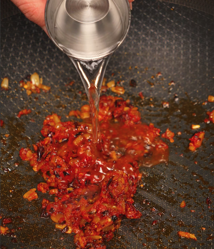 Vodka being poured into a pan with sautéed garlic, onions, and chili oil — creating the base for creamy chili oil vodka pasta sauce.