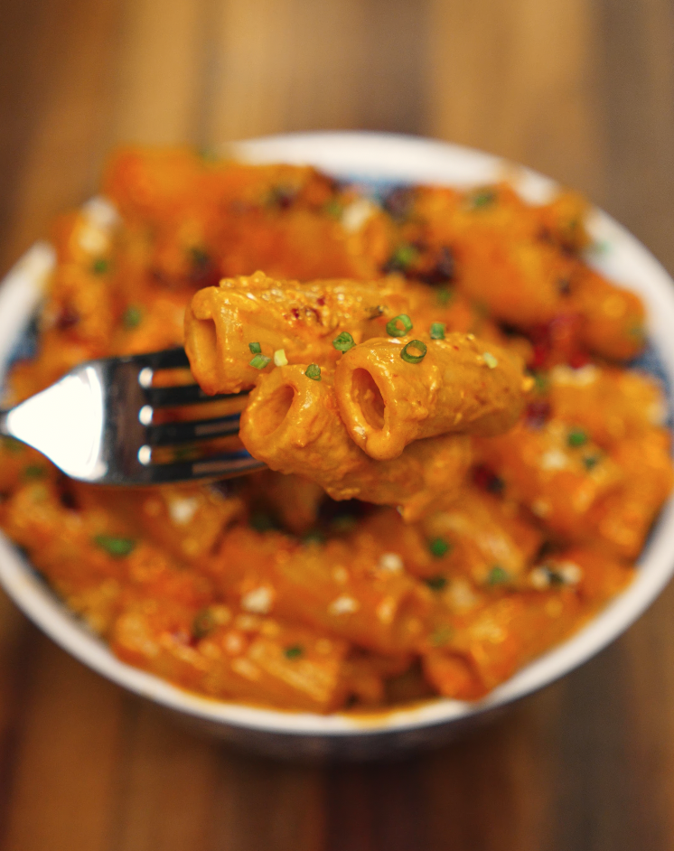 Close-up of creamy chili oil vodka pasta on a fork, garnished with chopped chives — spicy rigatoni pasta with a Korean-Italian twist.