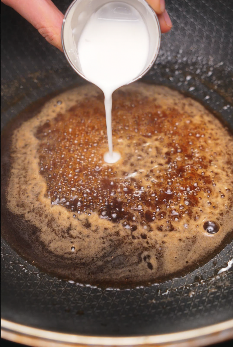 A cornstarch slurry being poured into a bubbling soy-based sauce in a skillet, creating the glossy and sticky glaze that coats the beef.