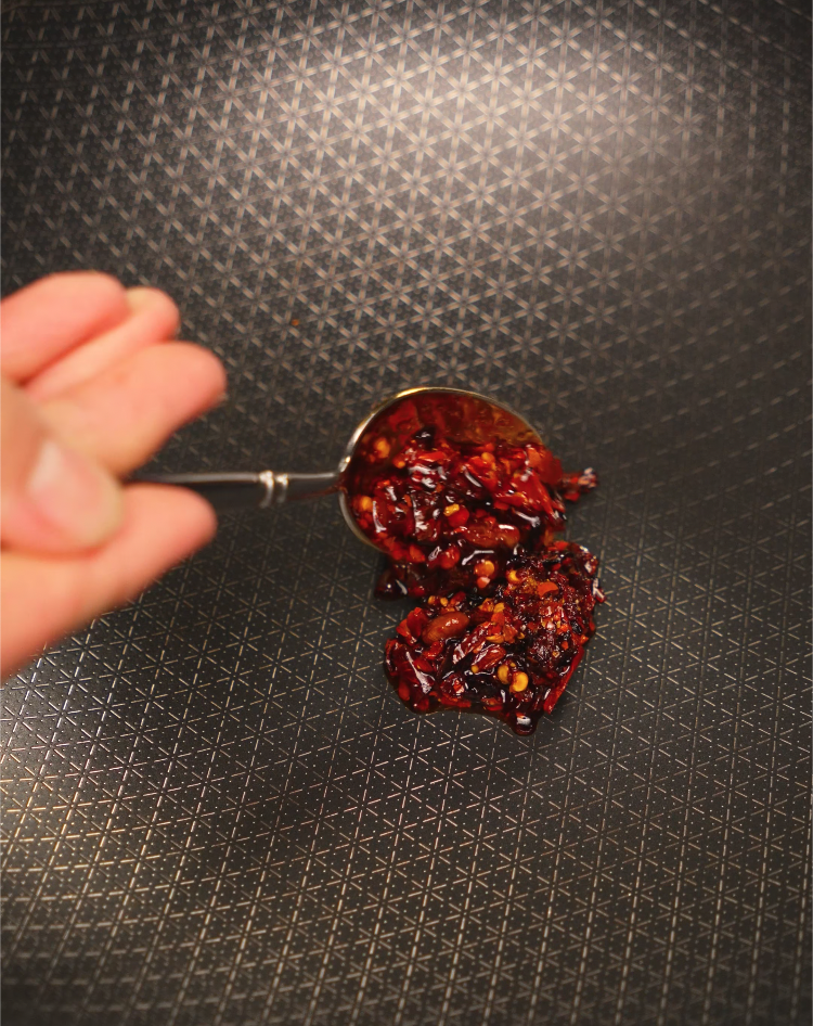 Spoonful of chili crisp being added to hot pan — bold flavor kick for spicy chili oil vodka pasta.