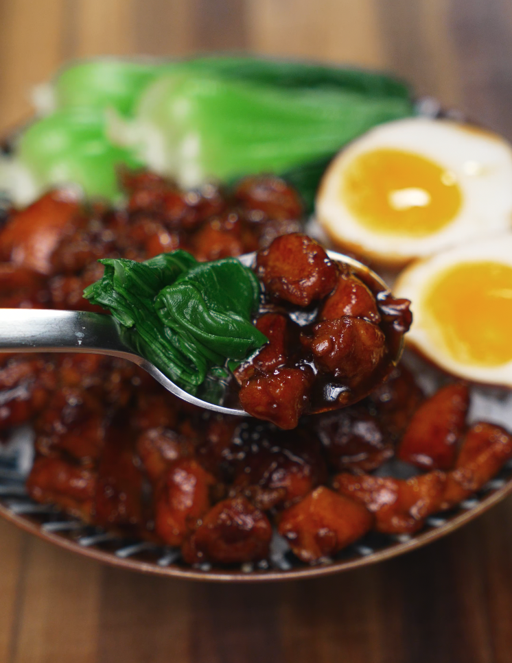 Close-up spoonful of Coca Cola braised chicken and bok choy lifted from a bowl with soft-boiled eggs and rice — sweet and savory chicken bowl idea.