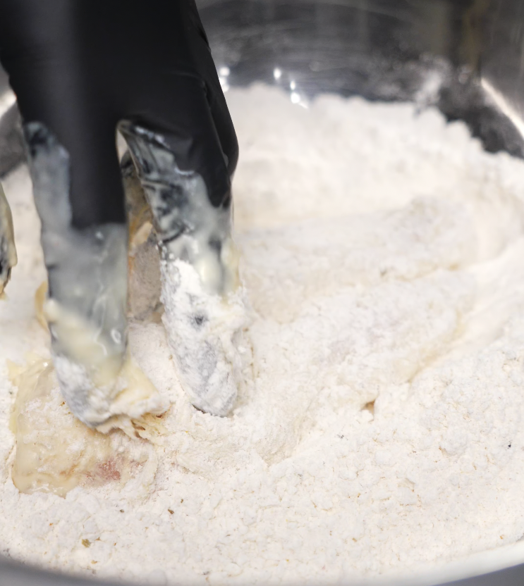 A hand lightly pushing down seasoned honey butter chicken tenders marinated in buttermilk to help tenderize it in order to get a super crispy exterior