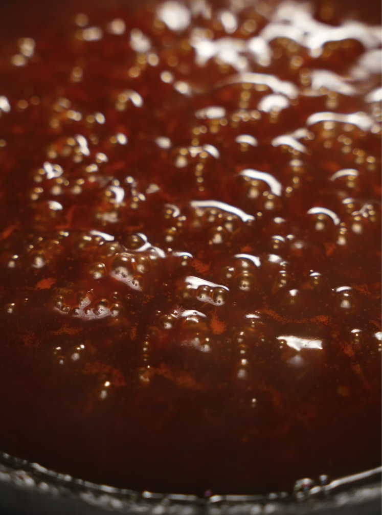 A deep red gochujang-based sauce simmers intensely in the pan, thickened and glossy, full of rich color and visible spices.