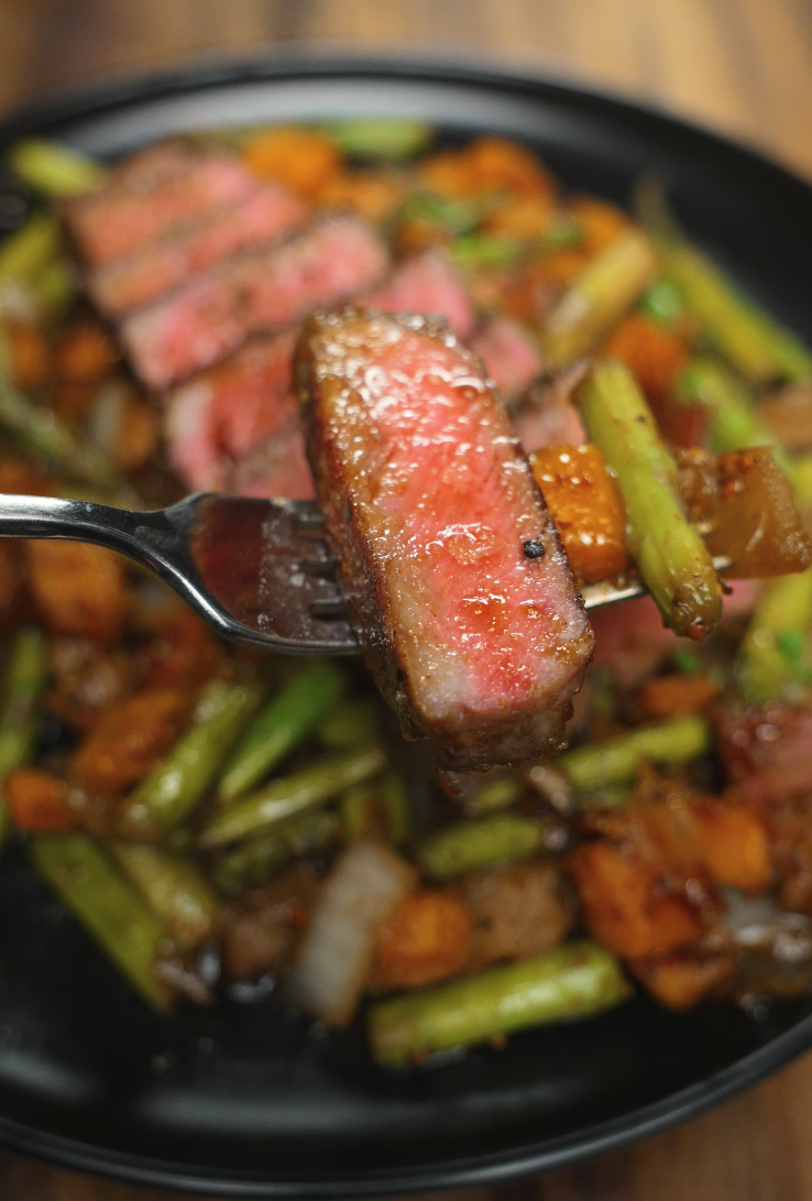 A tender, medium-rare steak is sliced on a wooden cutting board, revealing a juicy pink center. The crust is deeply seared and glistening with garlic butter, showcasing ideal doneness and texture.