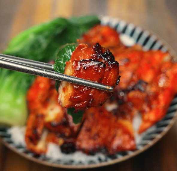 Close up of Char Siu Chicken being held by chopsticks
