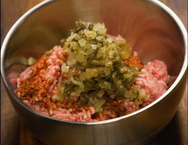 Ground pork mixed with pickled mustard greens and seasonings in a metal bowl — key topping for dan dan noodles.