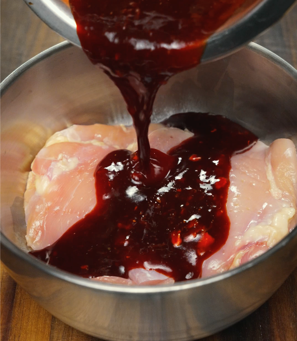 Pouring sweet and sticky char siu chicken marinade over chicken in metal bowl
