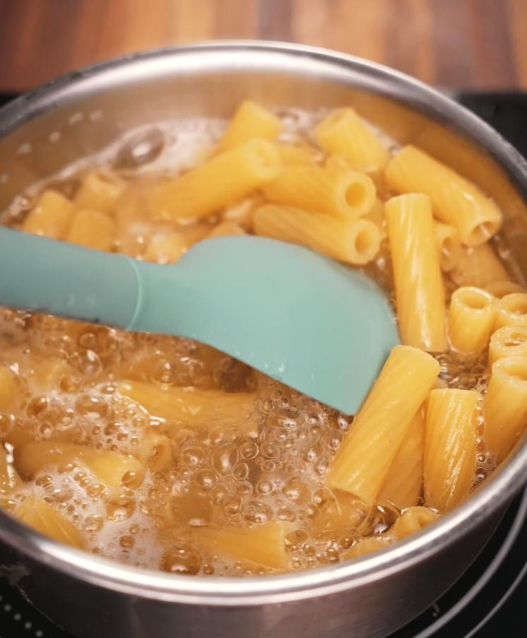 Rigatoni pasta boiling in a pot of salted water, stirred with a spatula to prevent sticking, capturing the essential step of cooking pasta for the dish.
