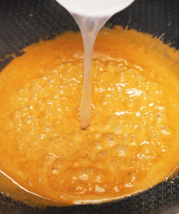 Pasta water being poured into a bubbling, spicy butter sauce in a pan, creating the creamy base for the spicy shrimp pasta sauce.