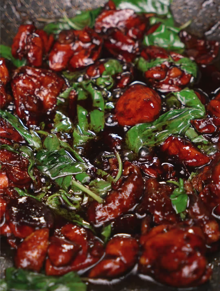 Fresh basil leaves visibly wilting into the thick, syrupy glaze that coats the chicken. This moment captures the melding of herbal and umami flavors at the heart of 3 Cup Chicken’s signature taste.