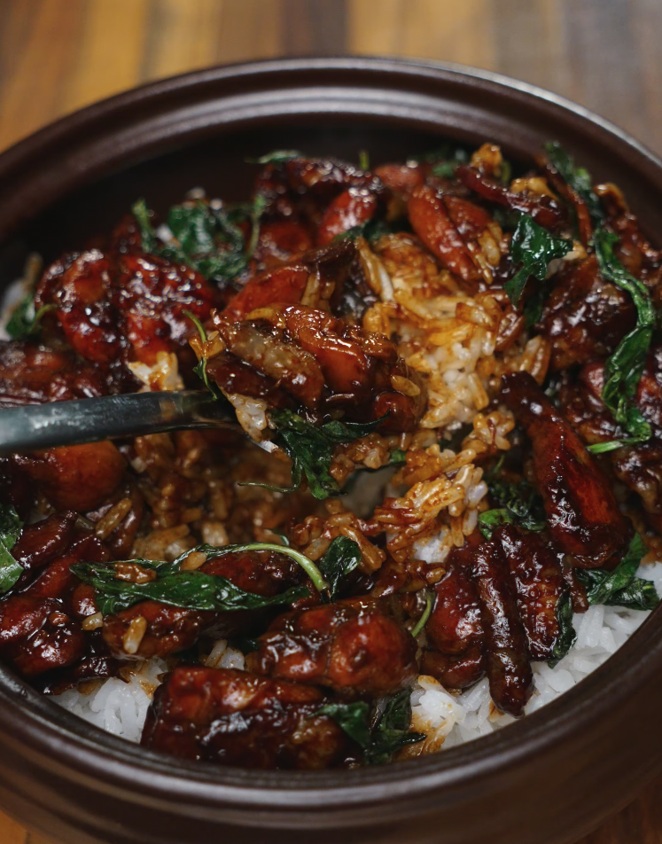 A spoon stirs through the 3 Cup Chicken, mixing saucy chicken chunks and fragrant basil into fluffy white rice. This image highlights how the sticky glaze clings to each grain, ensuring a deeply flavorful bite throughout.