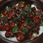 Final bowl of 3 Cup Chicken served over hot steamed rice in a clay pot, with glossy soy-based sauce coating the tender chicken and wilted basil leaves. This finished dish showcases the deep caramelized color, bold aroma, and sticky-sweet glaze typical of this Taiwanese classic.