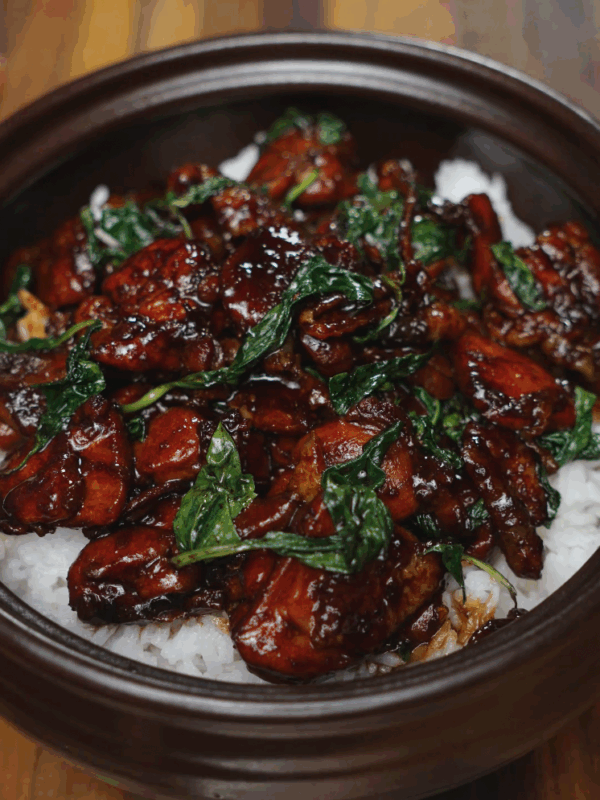 Final bowl of 3 Cup Chicken served over hot steamed rice in a clay pot, with glossy soy-based sauce coating the tender chicken and wilted basil leaves. This finished dish showcases the deep caramelized color, bold aroma, and sticky-sweet glaze typical of this Taiwanese classic.
