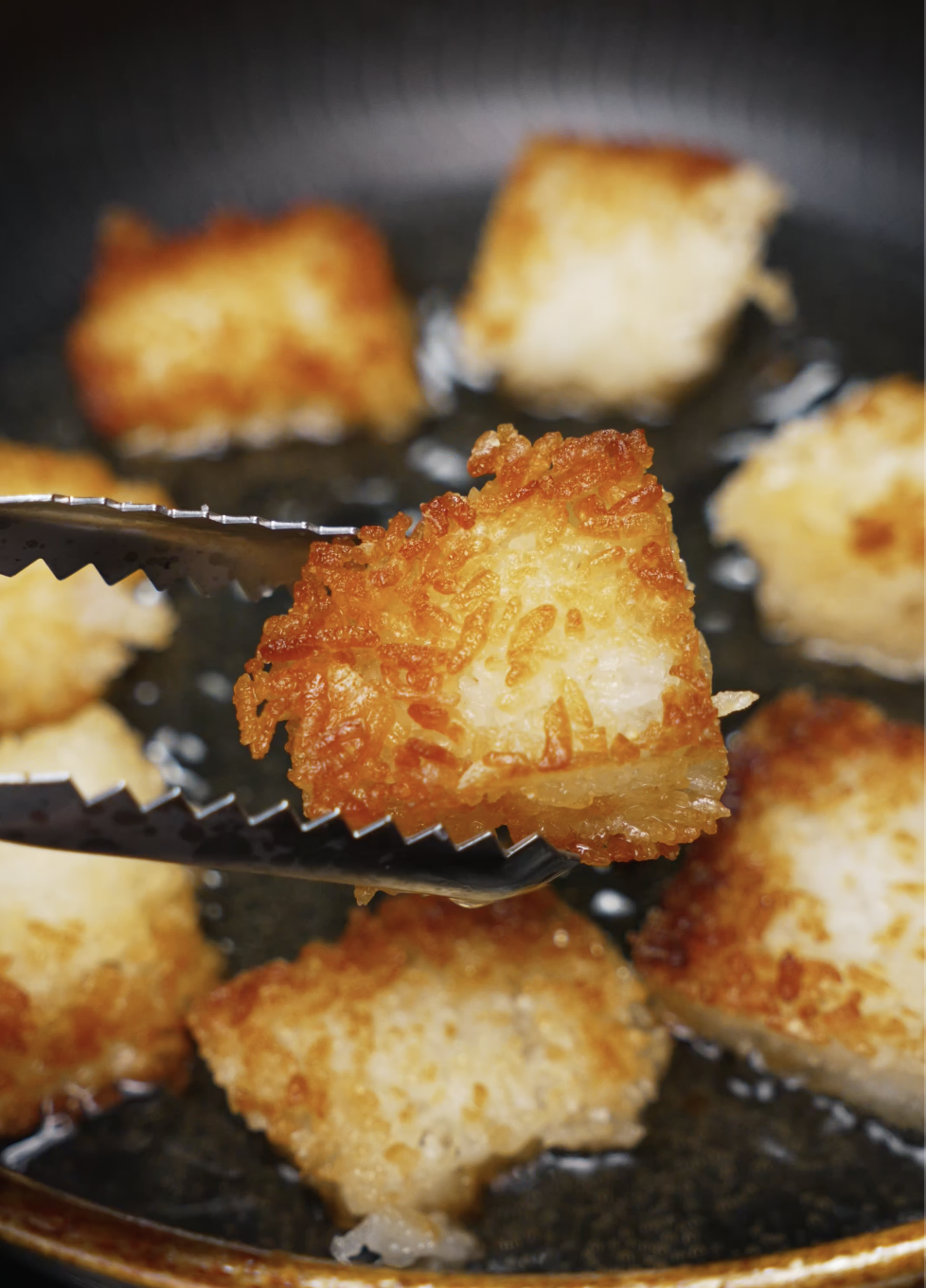 Golden brown rice cubes frying in oil with a close-up view of a crispy piece held by tongs. The exterior is perfectly crisp, making it the ideal base for spicy salmon toppings.