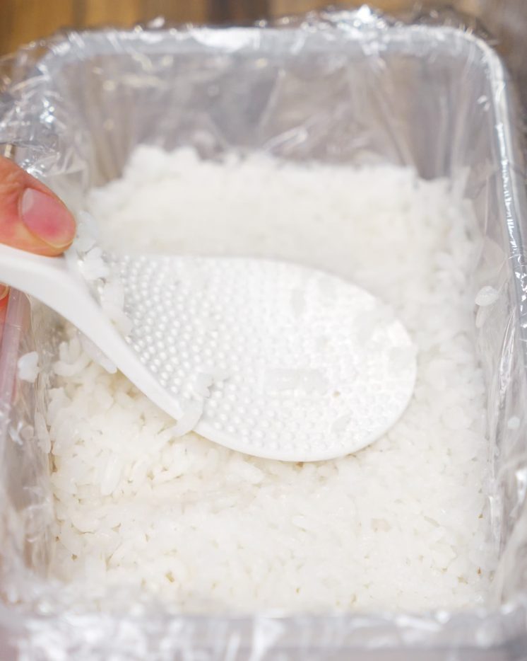 A rice paddle pressing down sushi rice in order to be frozen for an hour to make the rice cakes for Crispy Rice Salmon
