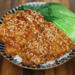 Soy garlic glazed chicken sliced and served over white rice with steamed bok choy on a ceramic plate. The chicken is coated in a glossy sweet and savory soy-based glaze and topped with toasted sesame seeds for texture and flavor.