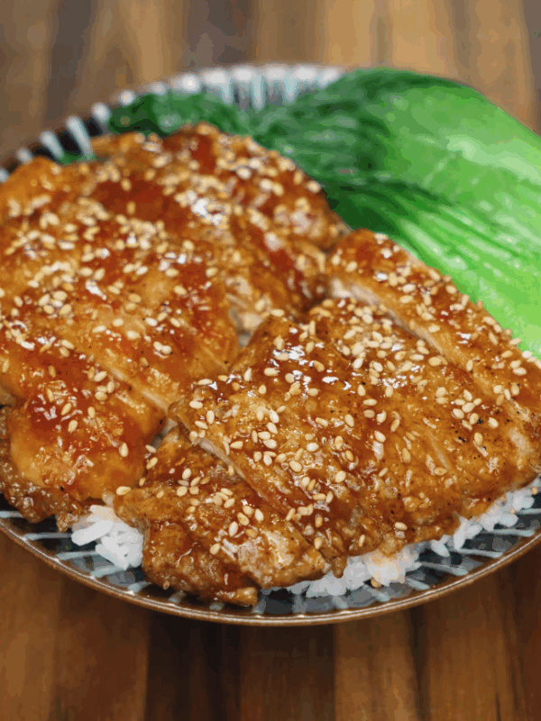 Soy garlic glazed chicken sliced and served over white rice with steamed bok choy on a ceramic plate. The chicken is coated in a glossy sweet and savory soy-based glaze and topped with toasted sesame seeds for texture and flavor.