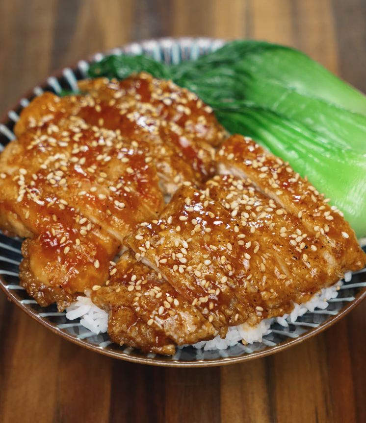 Soy garlic glazed chicken sliced and served over white rice with steamed bok choy on a ceramic plate. The chicken is coated in a glossy sweet and savory soy-based glaze and topped with toasted sesame seeds for texture and flavor.