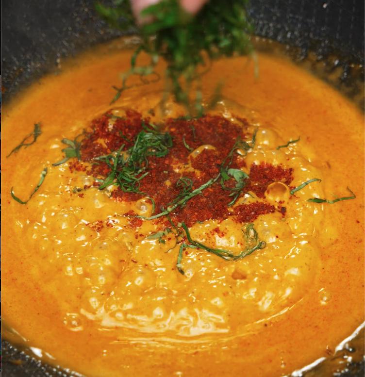 Chili powder and freshly sliced basil being added to the simmering gochujang Alfredo sauce, enhancing the heat and aromatic freshness of the dish.
